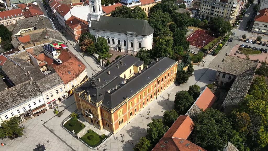 Pogled iz vazduha na gradski trg sa istorijskim zgradama, crkvom, sportskim terenima i uređenim ulicama