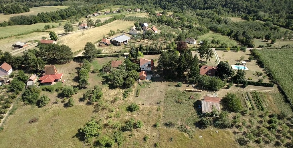 Pogled iz vazduha na selo sa kućama, dvorištima i poljoprivrednim parcelama okruženim zelenilom