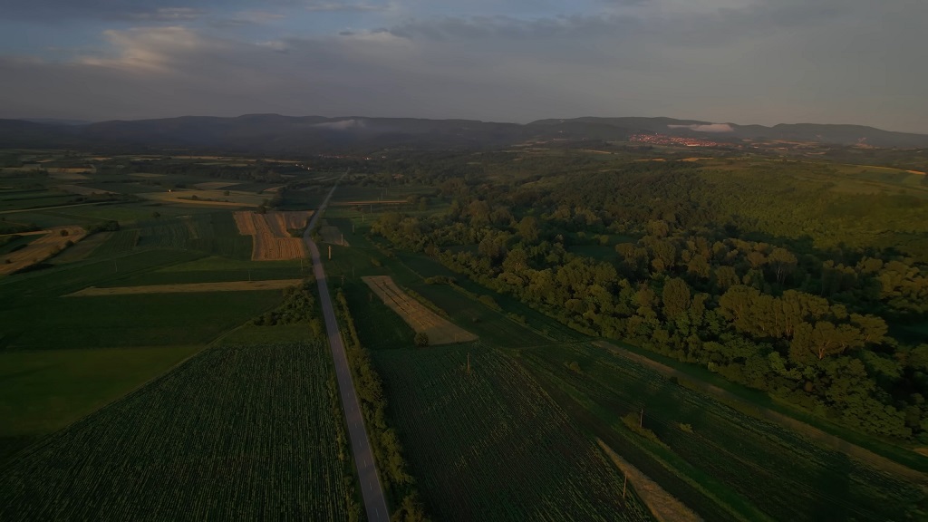 Panoramski pogled na poljoprivredne površine, šume i put kroz ruralni krajolik, snimljen u sumrak